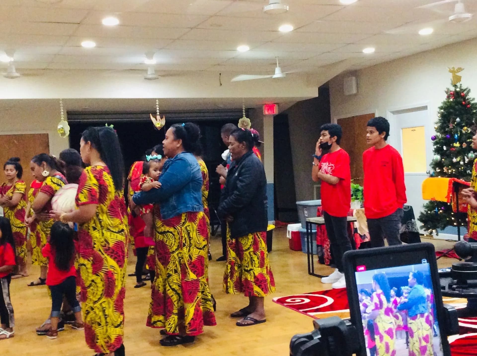Church members standing together in matching red and gold dress at a Christmas service, with a decorated tree behind them.