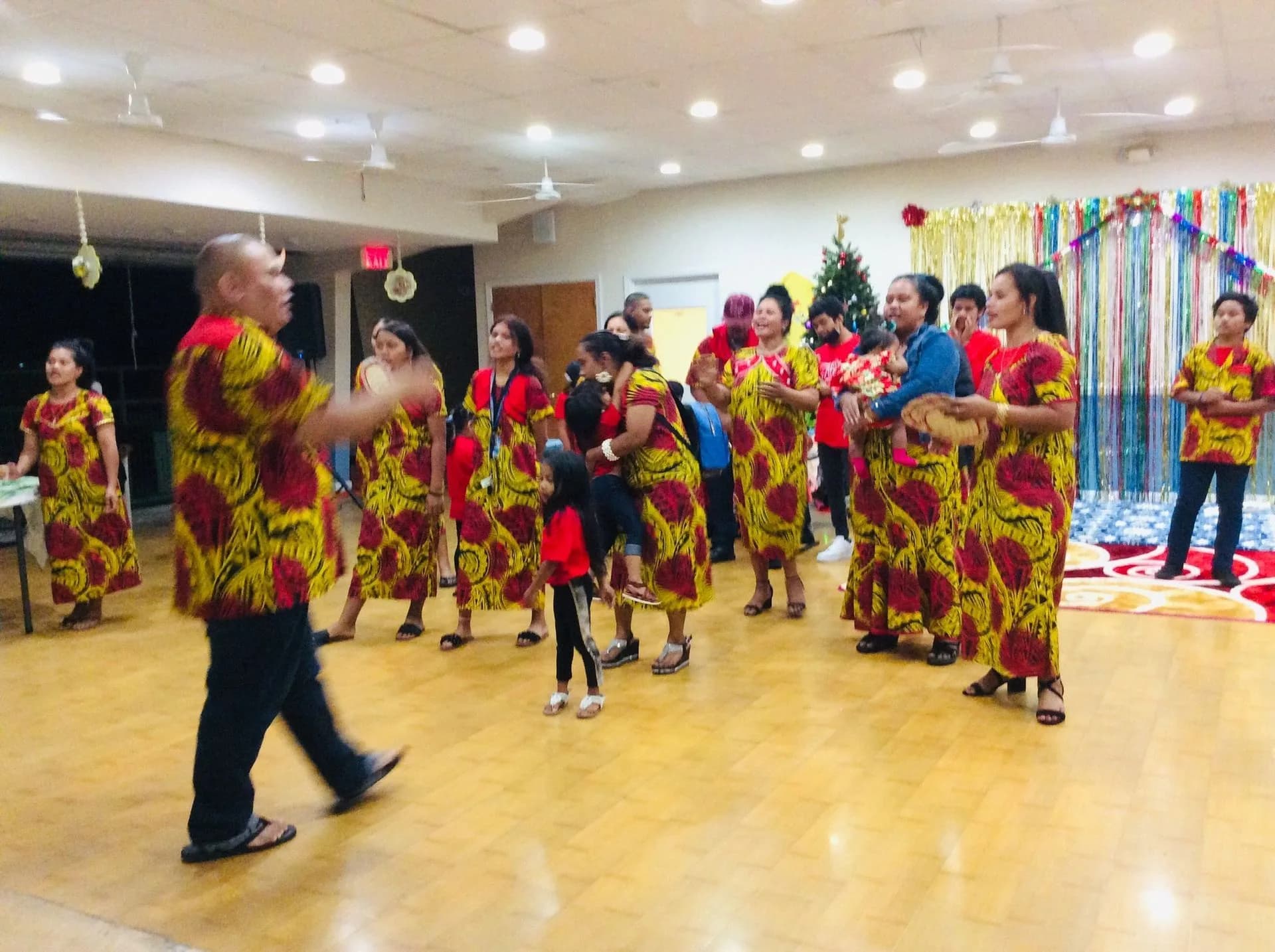 The whole congregation dancing together in matching red and gold island dress at a church celebration.